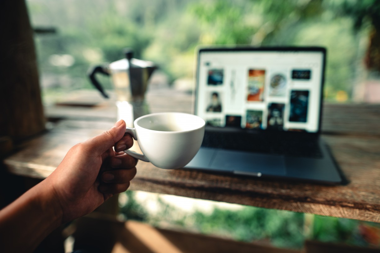 Person holding coffee cup up in front of their laptop, toasting to their website that is on the screen.