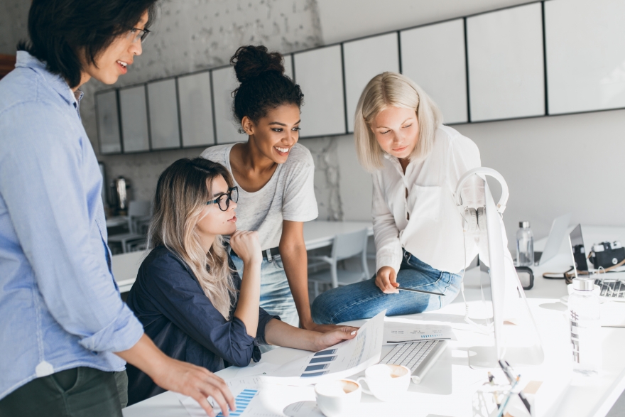 Group of business women browsing a laptop and reading through documents.