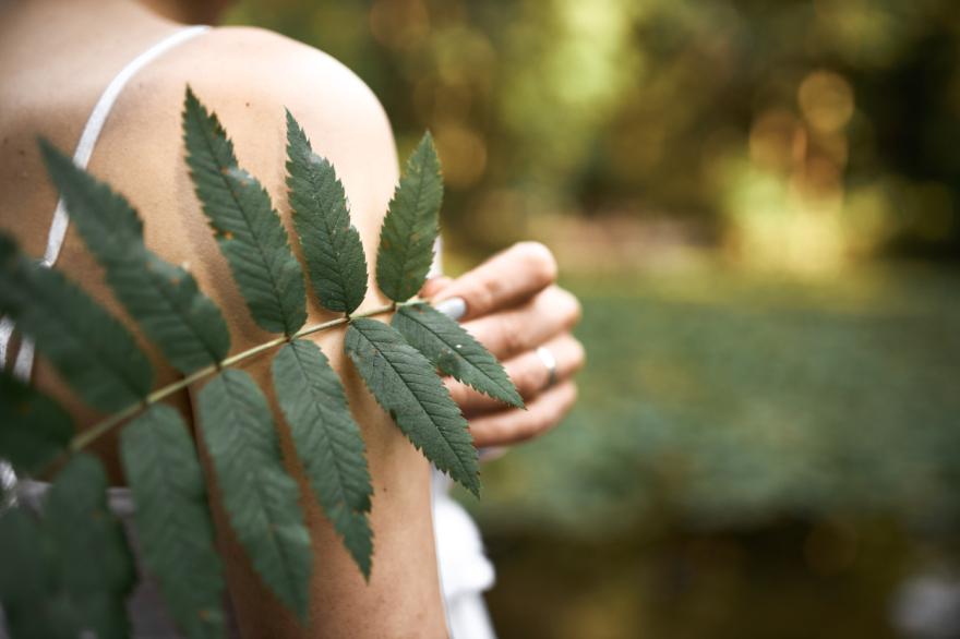 A woman holds a green leaf to her shoulder.