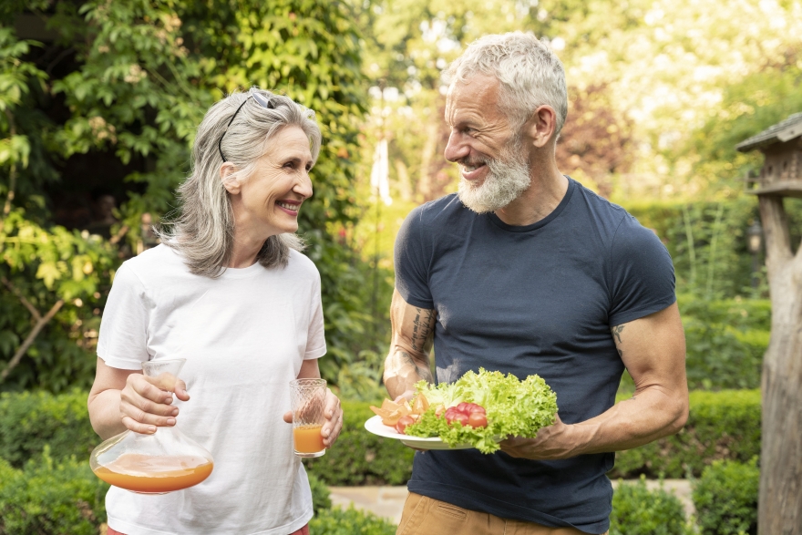 A couple of healthy older adults taking some time out of their busy lives to enjoy a nutritious salad and juice outside in the back yard. Nourishing the body and soul on their conscious living and self wellness journey.