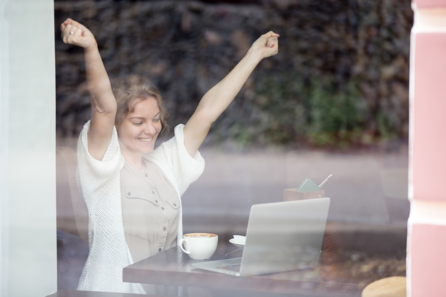 Woman having coffee in the window with arms raised feeling elevated.