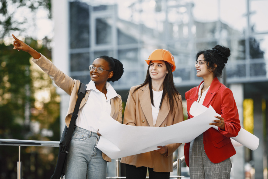 Three women engineers reviewing building plans on a construction site, symbolizing female leadership and collaboration in architecture and engineering.