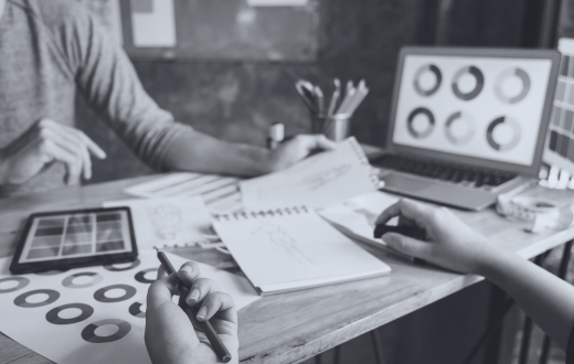 Two people sitting on opposite sides of a desk with brainstorming sketches and materials scattered around