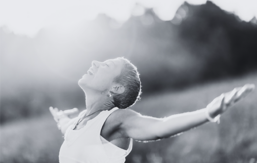 A woman stands in an open field, with her arms out wide in an empowered pose