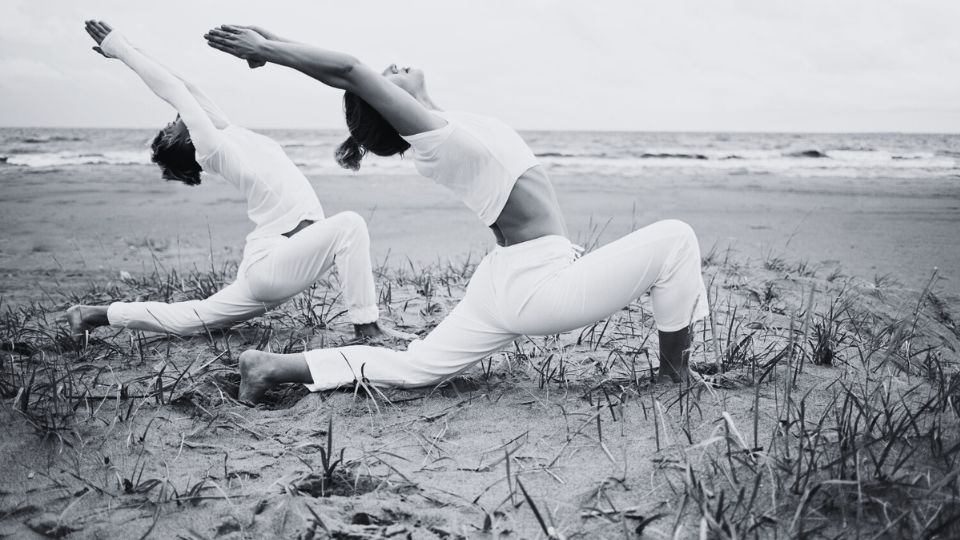 Two people in a warrior pose on the beach. Empowered with wellness concept.